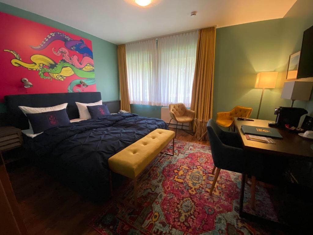 Habitación de hotel con cama, escritorio, silla, alfombra colorida y una ventana grande con cortinas.
