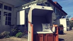 A small, enclosed wooden structure with a white canopy, a cushion with an anchor design, and a sign reading "Hotel Schönstein". - Hafen Hotel Schützenhof (Fehmarn)