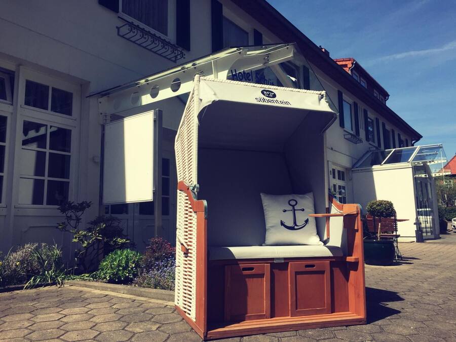 Una pequeña estructura de madera cerrada con un dosel blanco, un cojín con diseño de ancla y un letrero que dice "Hotel Schönstein".
