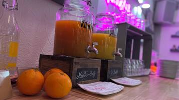 Un coin bar avec un panneau lumineux au néon, un grand bocal en verre rempli de jus d’orange et des oranges disposées sur le comptoir.