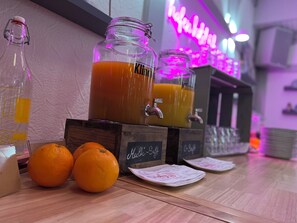 Zona de bar con un letrero de neón, un tarro grande de jugo de naranja y naranjas sobre la barra.