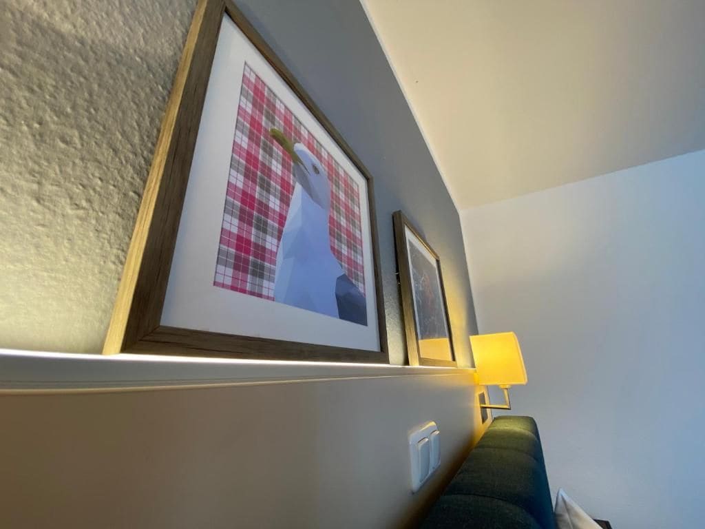 A hotel room with a wall-mounted shelf holding framed pictures, a bedside lamp, and a power outlet.