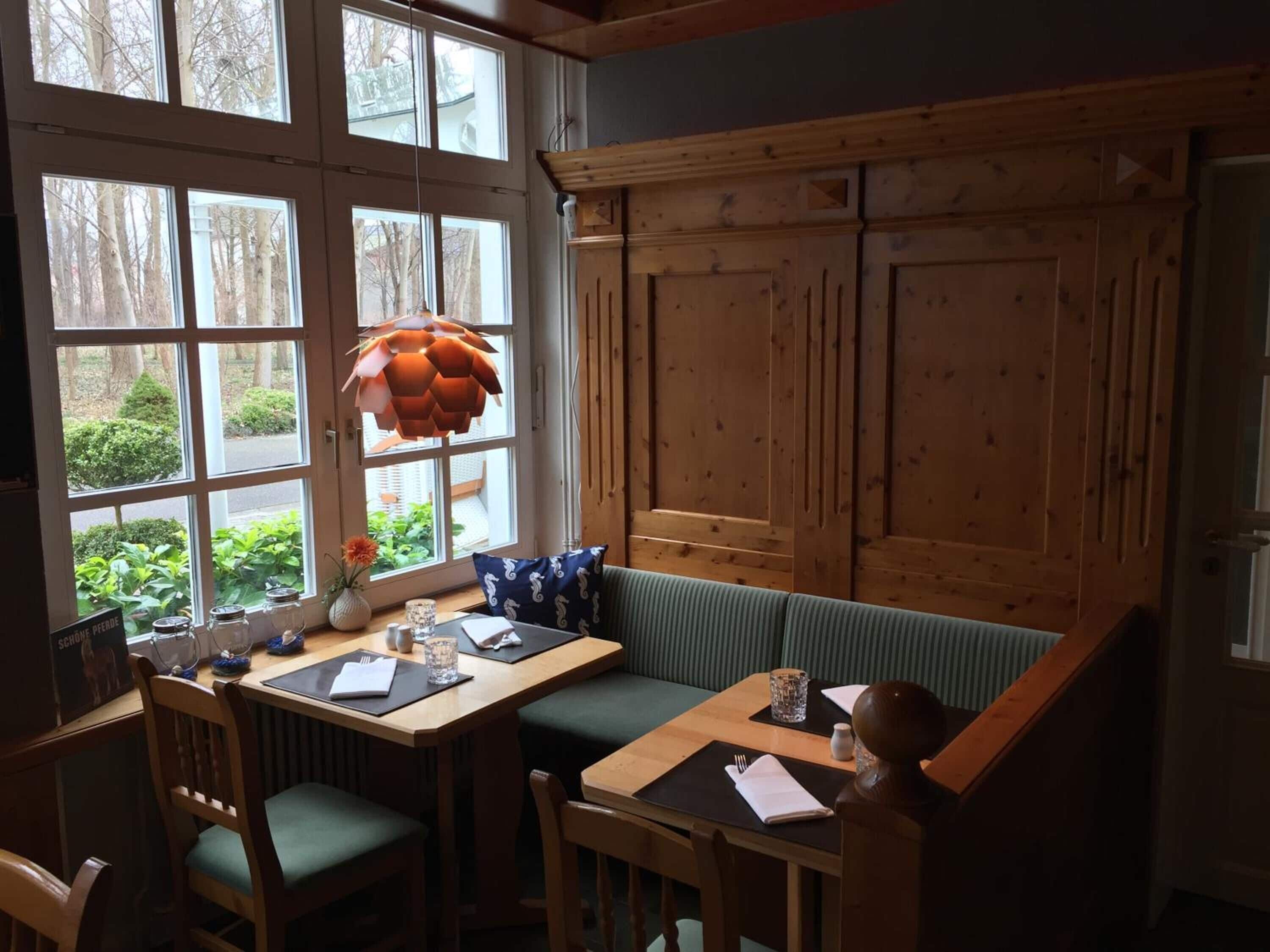 Un'accogliente zona pranzo con tavolo e panche in legno, ampie finestre con vista sugli alberi e un lampadario arancione a sospensione.