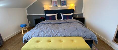 Un dormitorio con cama, un banco, una mesita de noche y una lámpara.