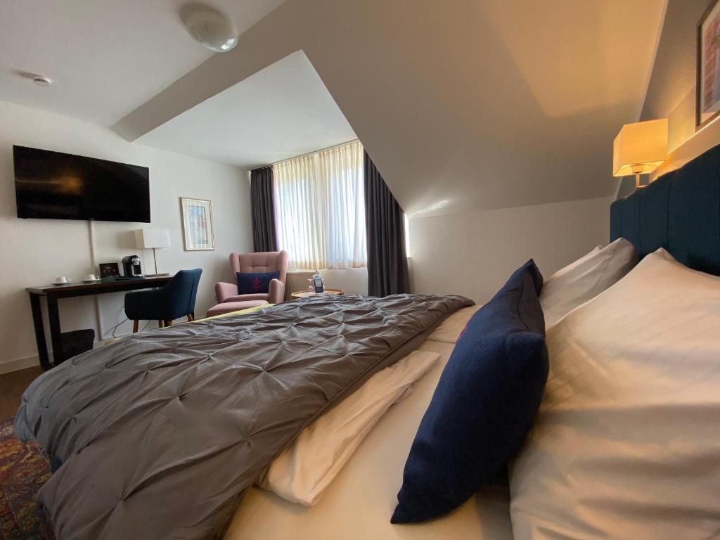 A hotel room with a bed, a desk, a chair, a television, and a window with curtains.