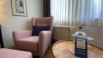 Ein Hotelzimmer mit einem rosafarbenen Sessel, einem Holztischchen mit Wasserspender und einem gerahmten Bild an der Wand.