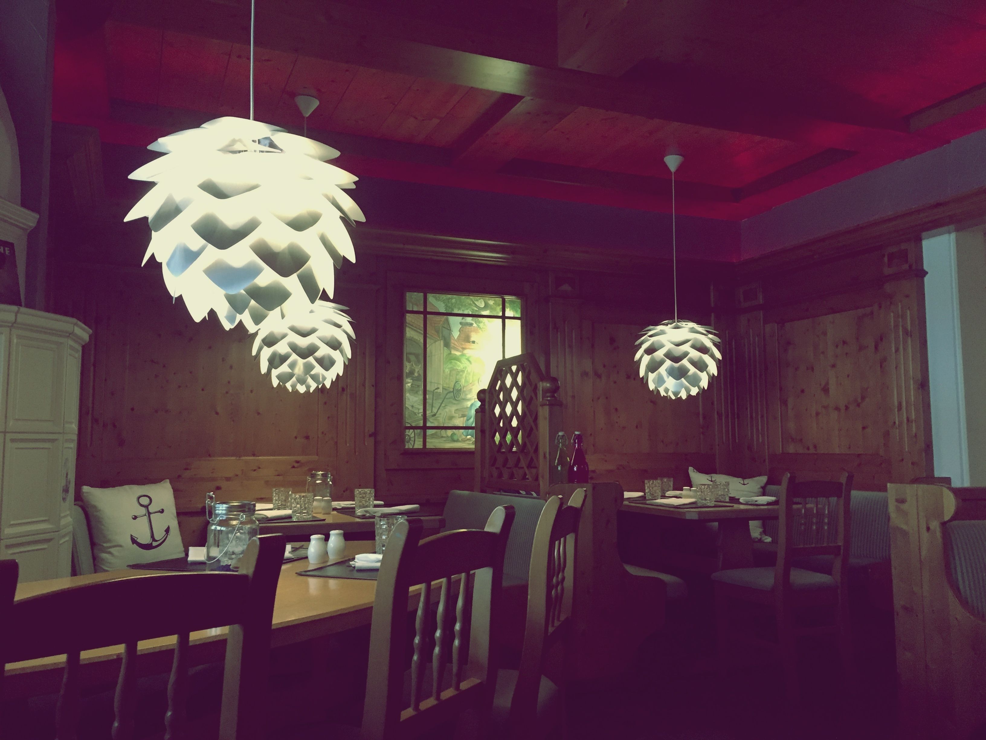 A dining area with wooden walls, a large window, and hanging pendant lights.