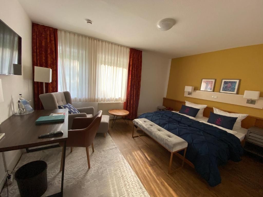 A hotel room with a bed, a desk, a chair, a small table, and a bench.
