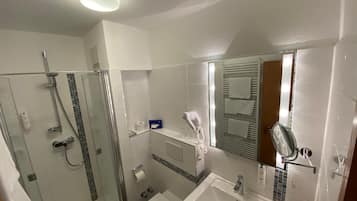 Un baño moderno con ducha de vidrio, lavamanos blanco y espejo con toallero.