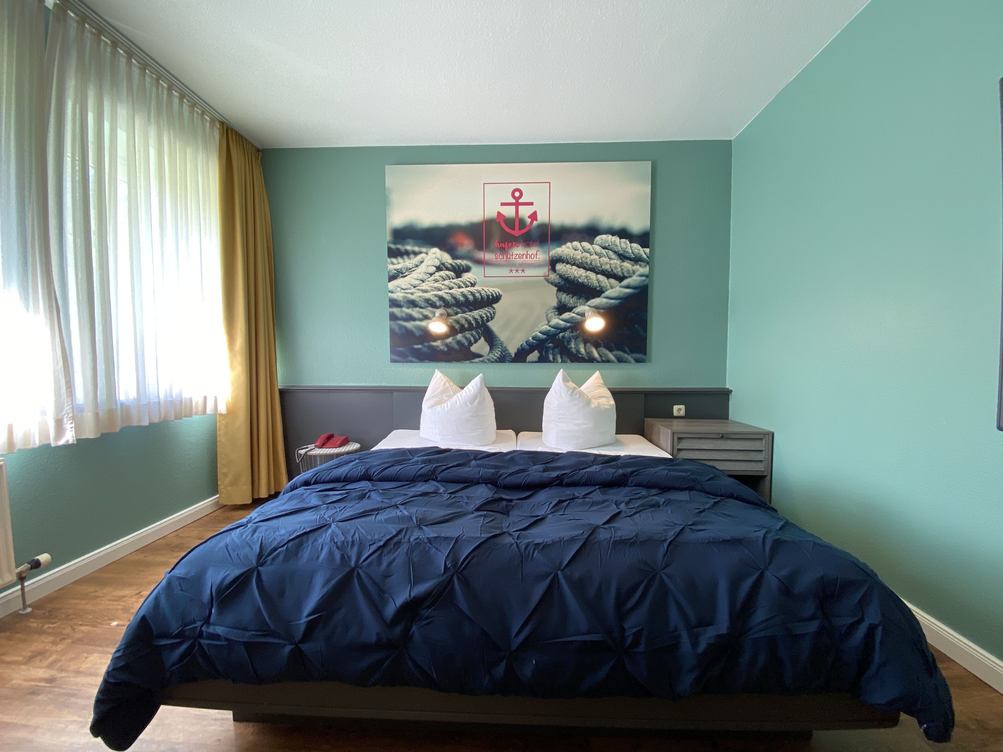 A bedroom with a large bed, a headboard, a nightstand, and a wall-mounted artwork of a rope and anchor.