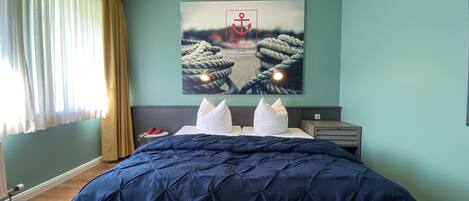 A bedroom with a large bed, a headboard, a nightstand, and a wall-mounted artwork of a rope and anchor.
