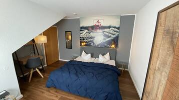 A bedroom with a bed, a desk, a chair, a mirror, and a painting of ropes on a wall.