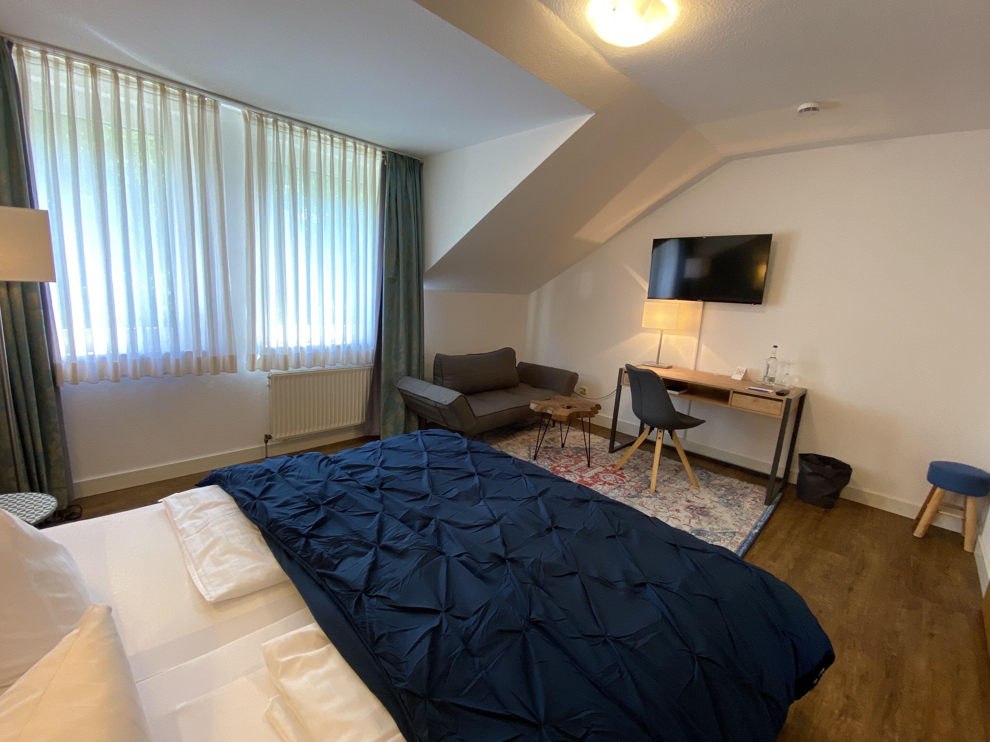 A hotel room with a bed, a desk, a chair, a TV, and a window with curtains.