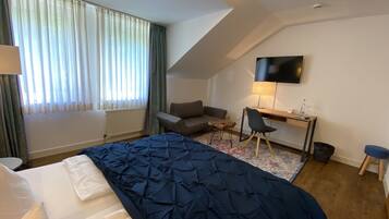A hotel room with a bed, a desk, a chair, a TV, and a window with curtains.