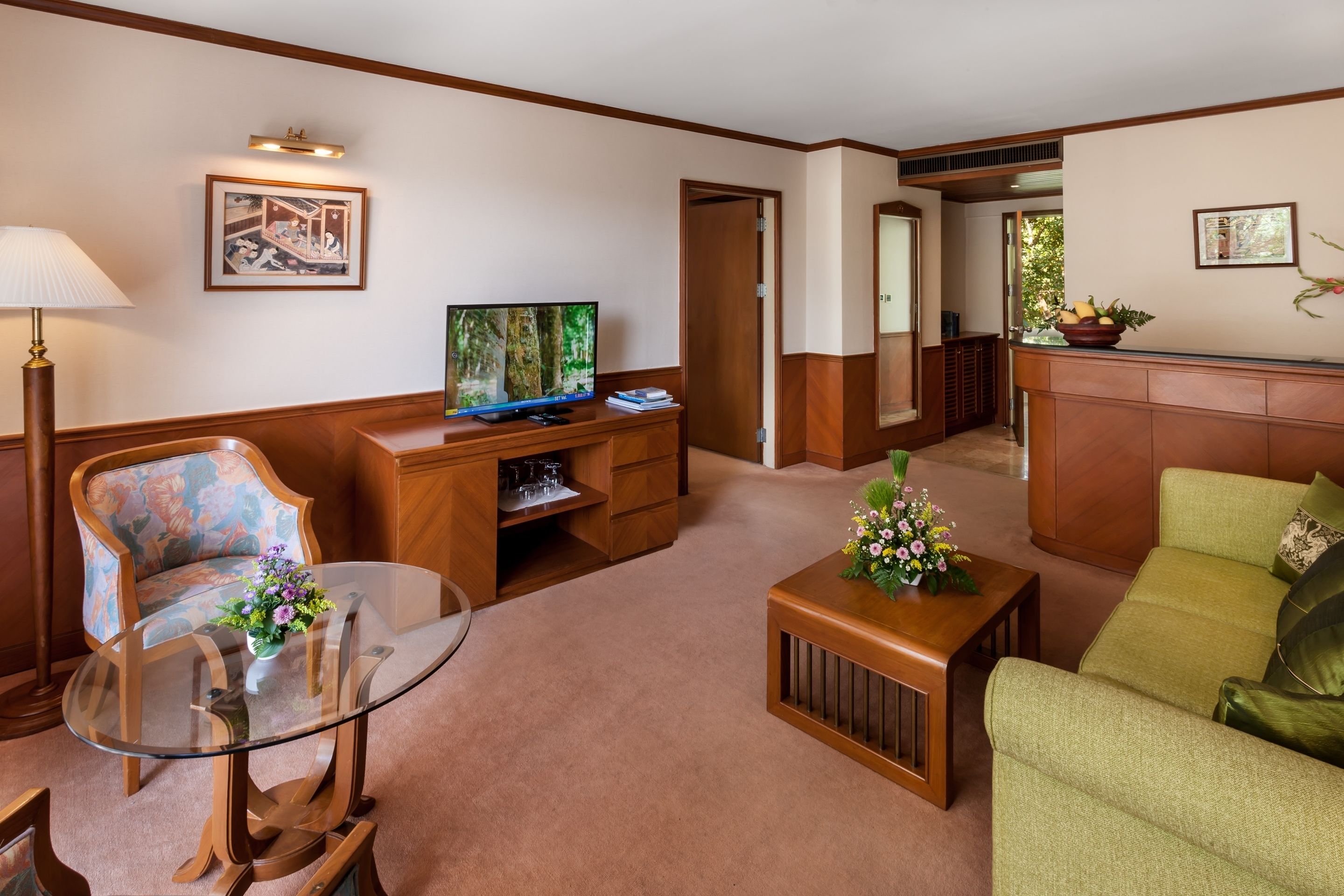 Una sala de estar con televisor, una mesa de centro de vidrio, un sofá, un sillón y un jarrón decorativo.