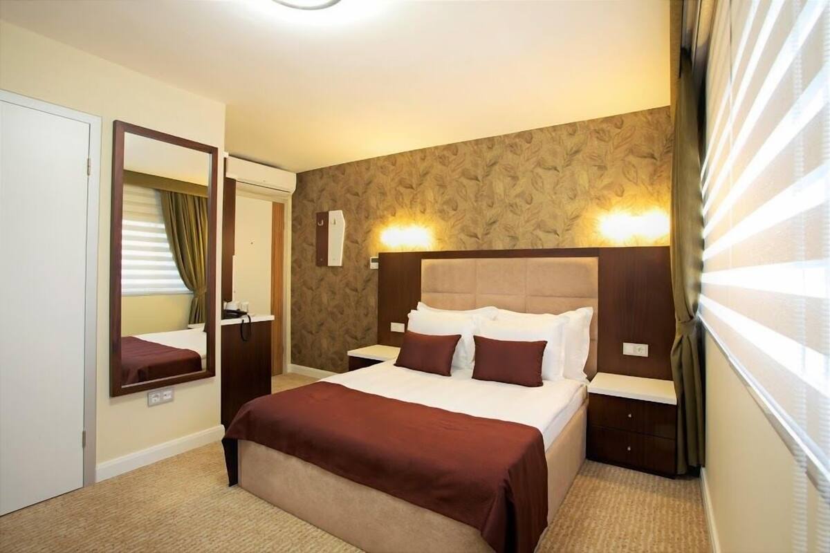 A hotel room with a large bed, a bedside table, a mirror, and a wall-mounted light fixture.