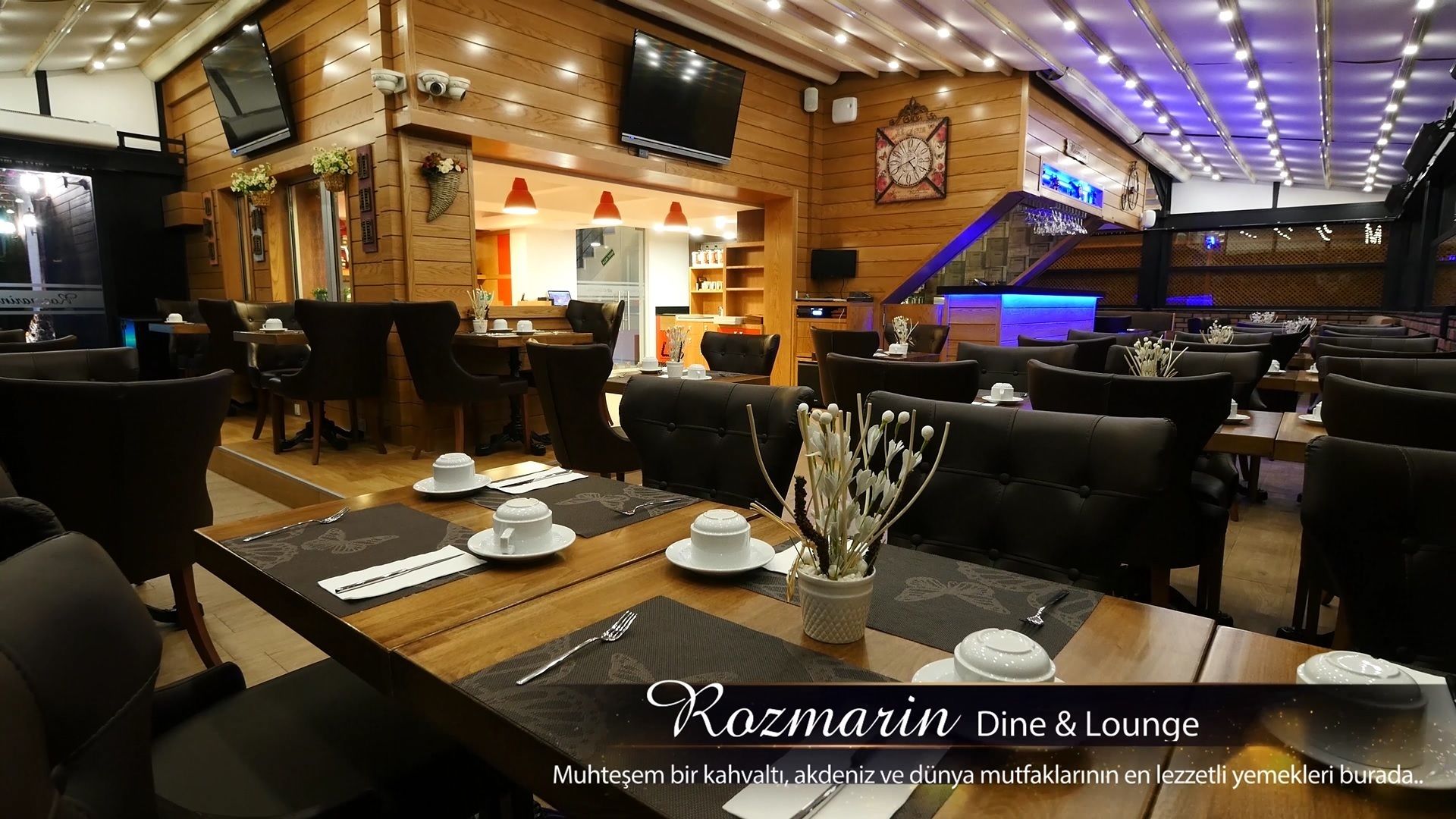 A cozy restaurant with wooden decor and comfortable seating. Tables are set with white plates and silverware.