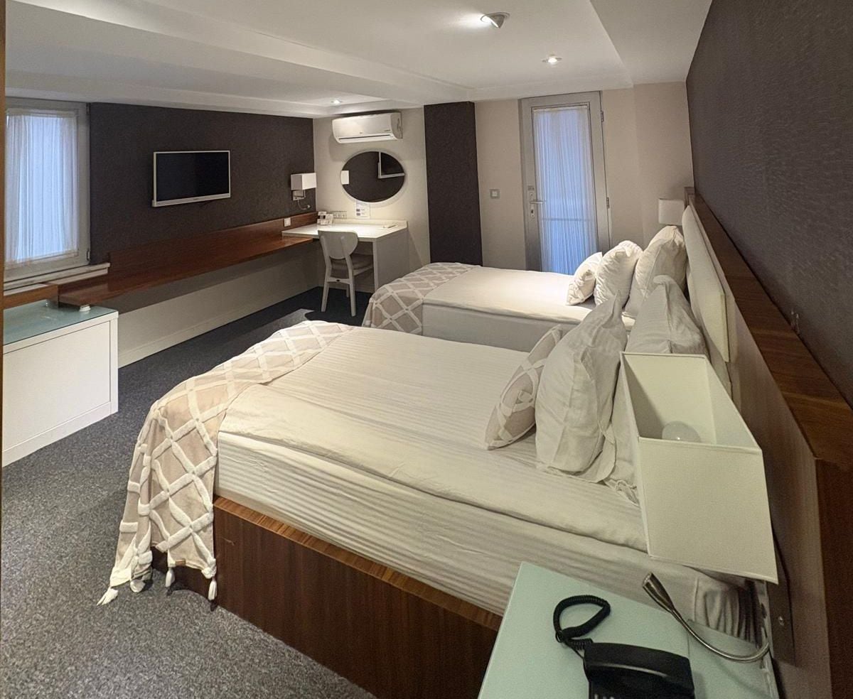 Ein Hotelzimmer mit zwei Betten, einem Schreibtisch, einem Stuhl, einem Fernseher und einem Badezimmer.