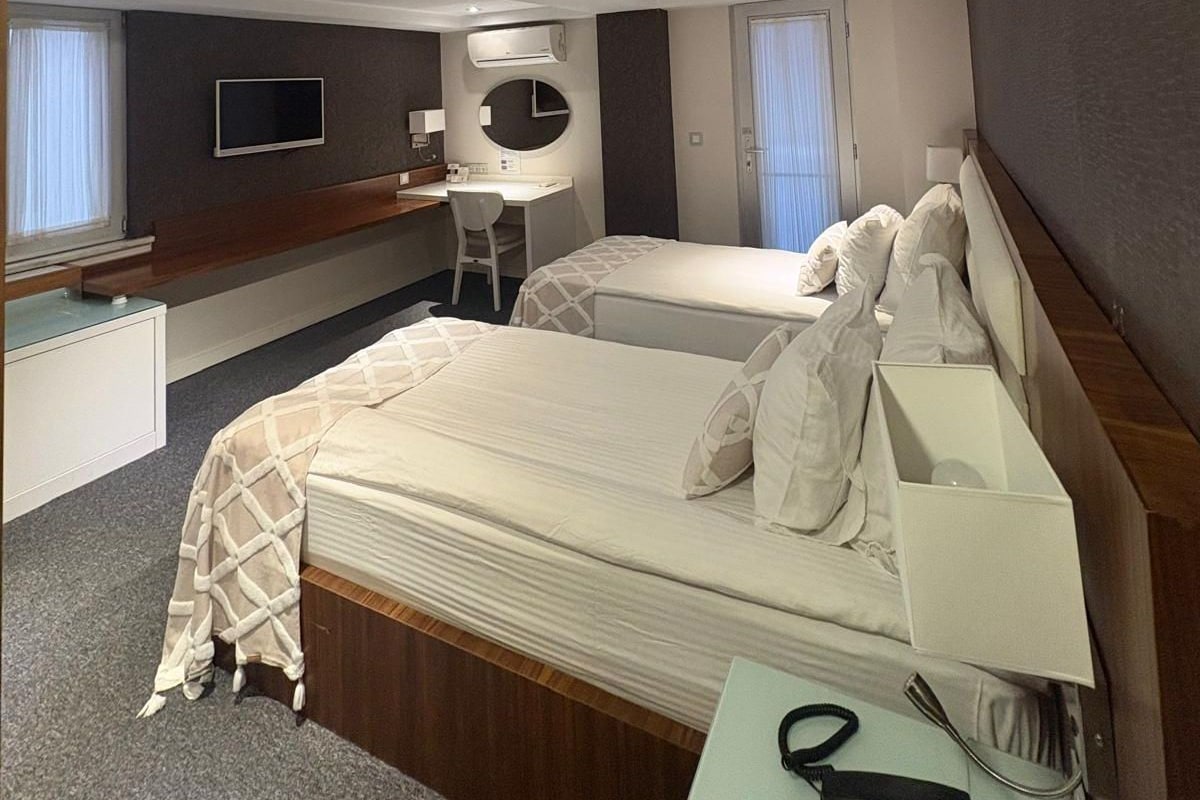 A hotel room with two beds, a desk, a chair, a TV, and a bathroom.