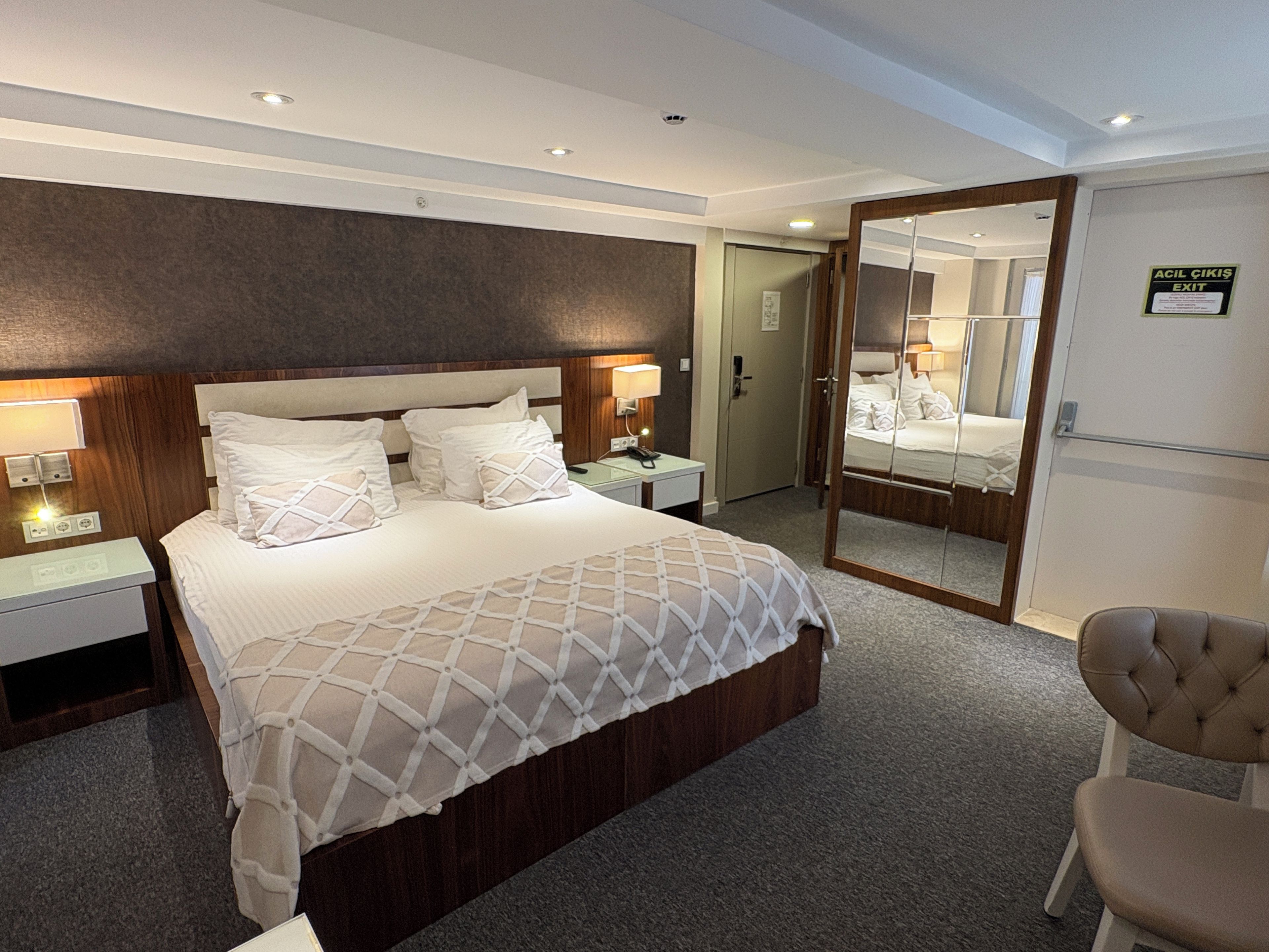 A hotel room with a large bed, bedside tables, a mirror, and a chair.