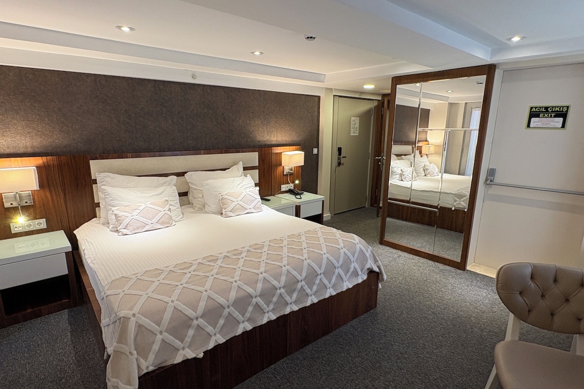 A hotel room with a large bed, bedside tables, a mirror, and a chair.