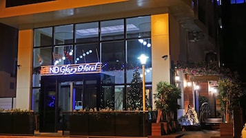 Exterior del hotel ND Glory, con fachada de vidrio moderna, señalización iluminada y un área de entrada bien iluminada con plantas en macetas.
