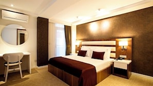 A hotel room with a bed, bedside tables, a desk, a chair, a round mirror, and an air conditioning unit. - End Glory Hotel (Corlu)