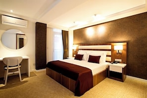A hotel room with a bed, bedside tables, a desk, a chair, a round mirror, and an air conditioning unit. - End Glory Hotel (Corlu)