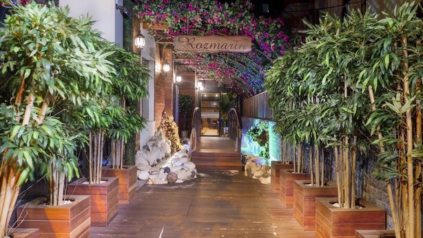 Uma passarela de madeira leva à entrada de um edifício, onde se lê a placa