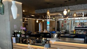L’intérieur d’un restaurant, avec des tables dressées pour le service, un bar où sont exposées des bouteilles et des lampes suspendues.