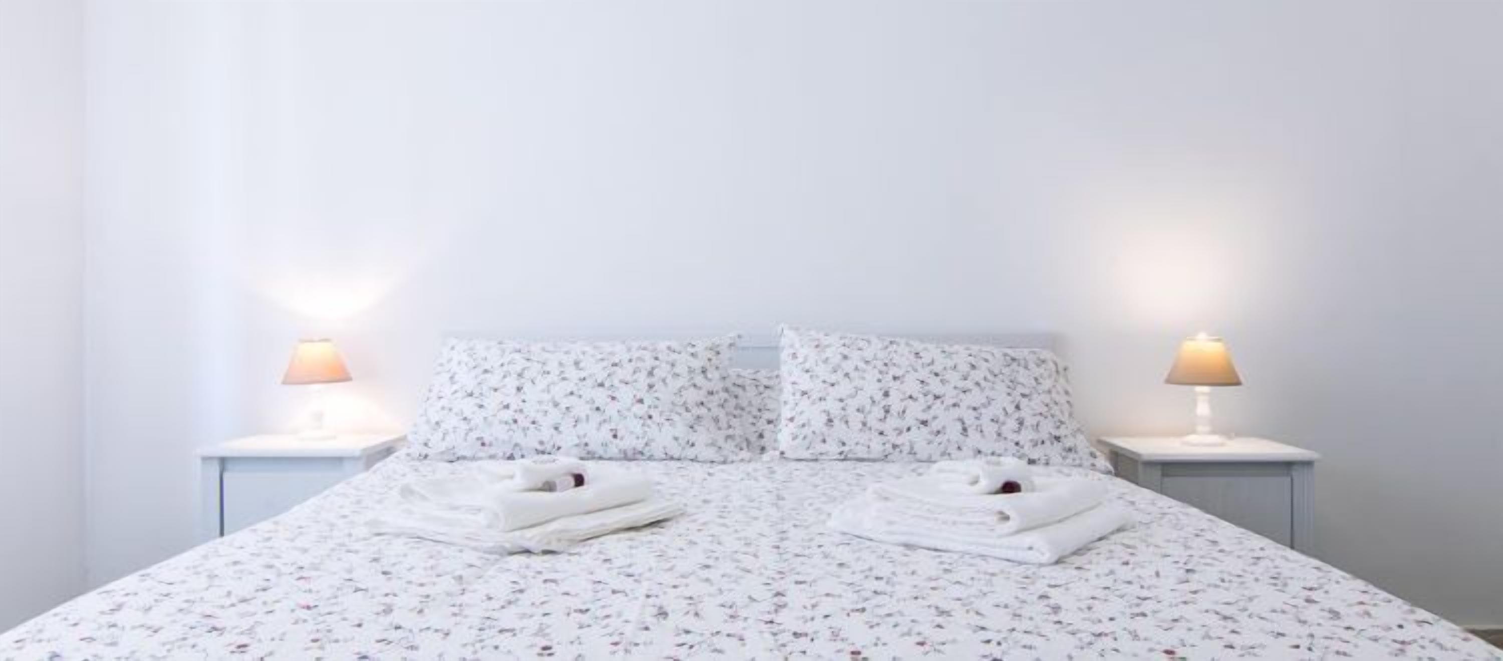 A neatly made bed with floral bedding, two bedside lamps, and folded towels on the bed.