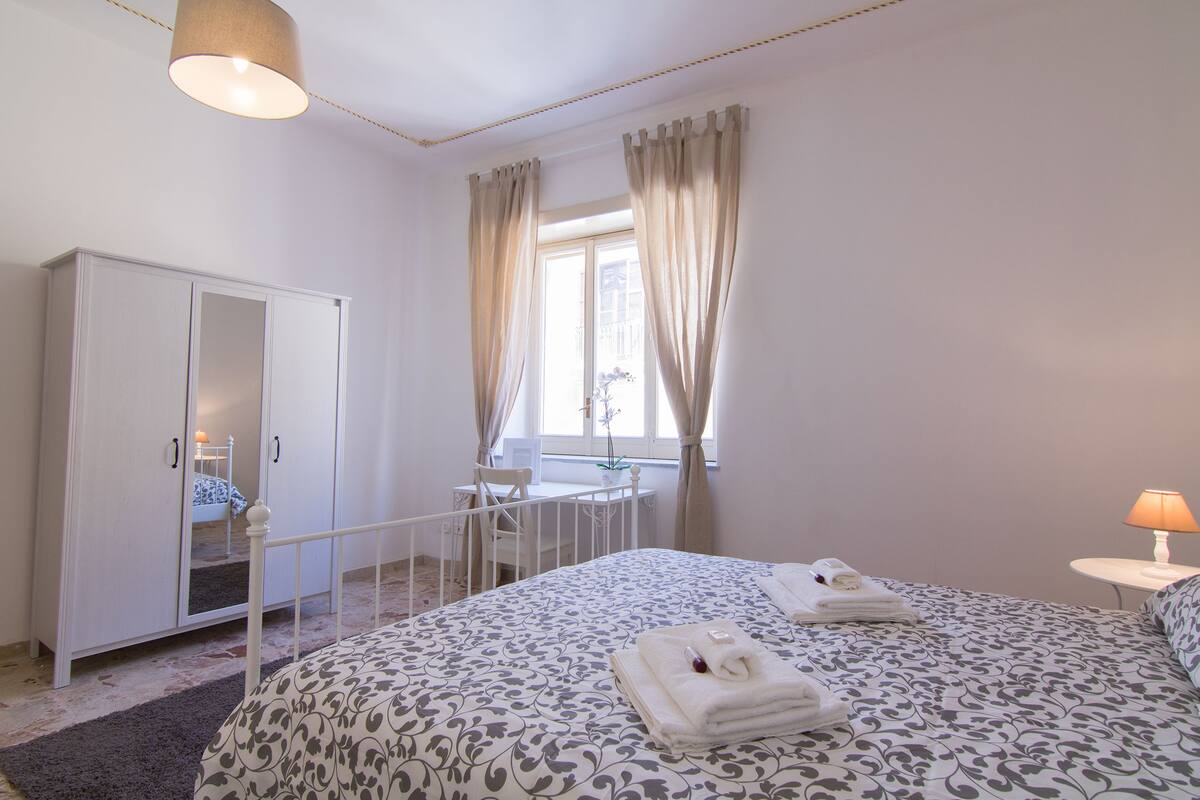 A bedroom with a bed, a wardrobe, a desk, and a window with curtains.