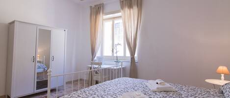 A bedroom with a bed, a wardrobe, a desk, and a window with curtains.