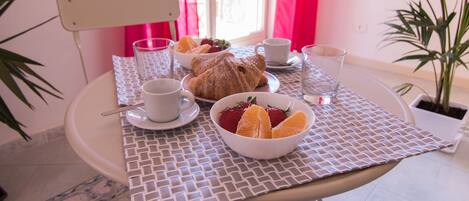 A dining table with a white tablecloth, a bowl of strawberries, a croissant, and a glass of water.