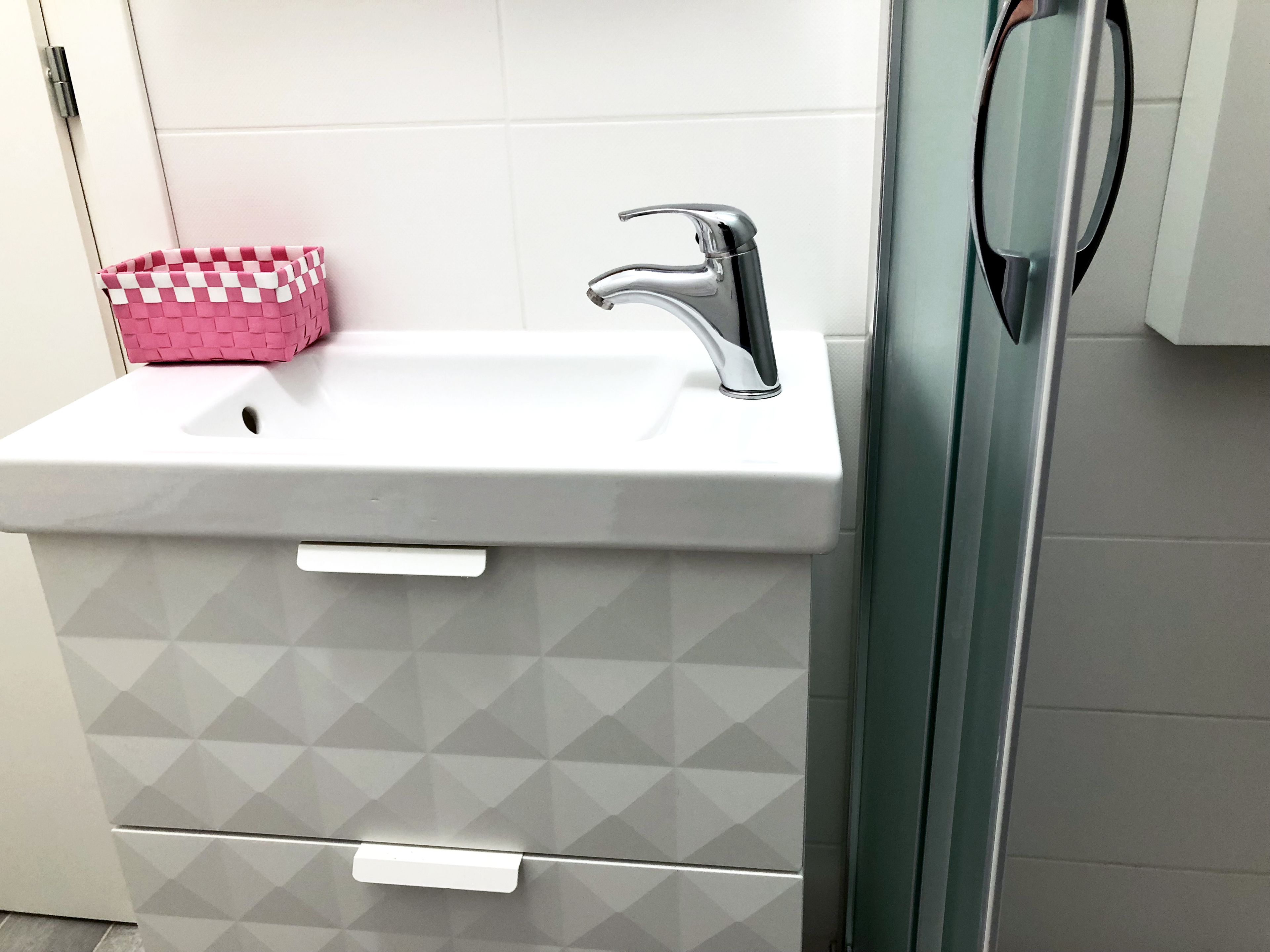 A bathroom with a white sink, a pink basket, and a green door.