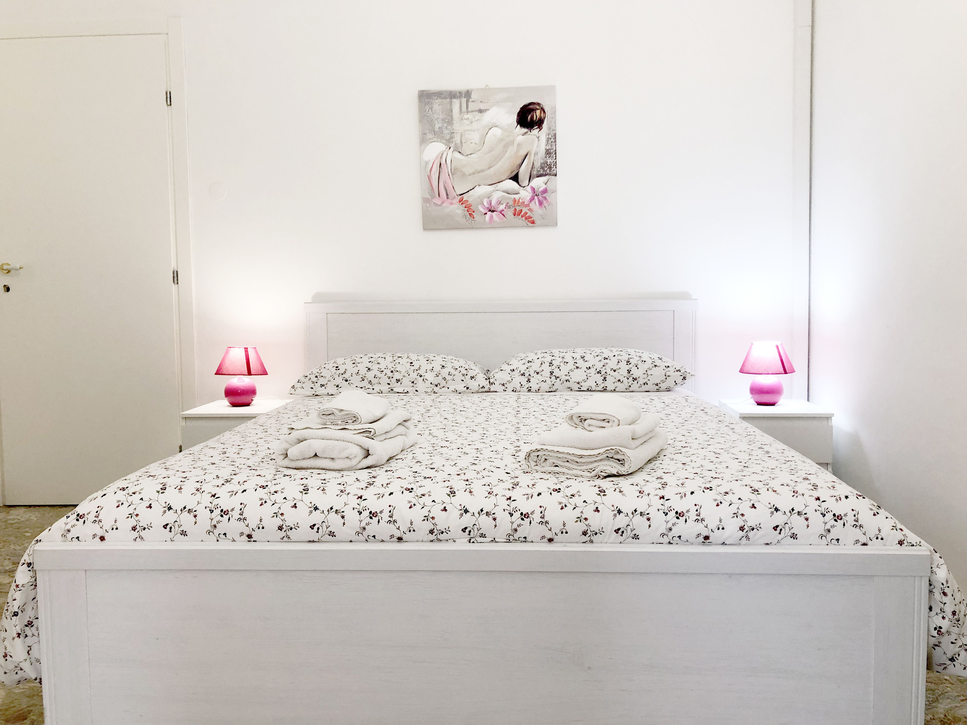 A bedroom with a bed, two bedside lamps, a painting, and folded towels on the bed.