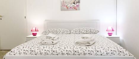 A bedroom with a bed, two bedside lamps, a painting, and folded towels on the bed.