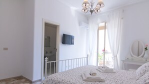 A bedroom with a bed, a TV, a mirror, and a balcony with a view.