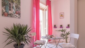 A room with a dining table, chairs, potted plants, and a painting on the wall.