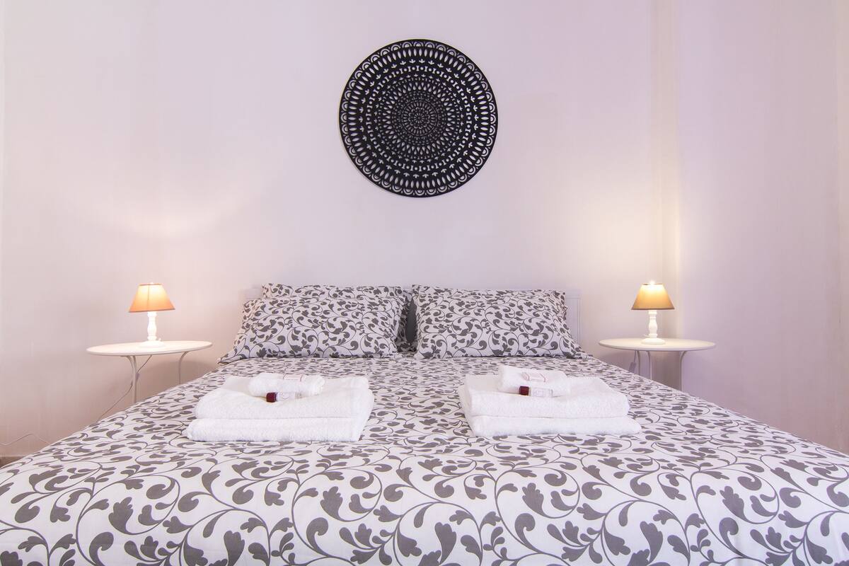 A double bed with patterned bedding, two bedside lamps, and a circular wall decoration.