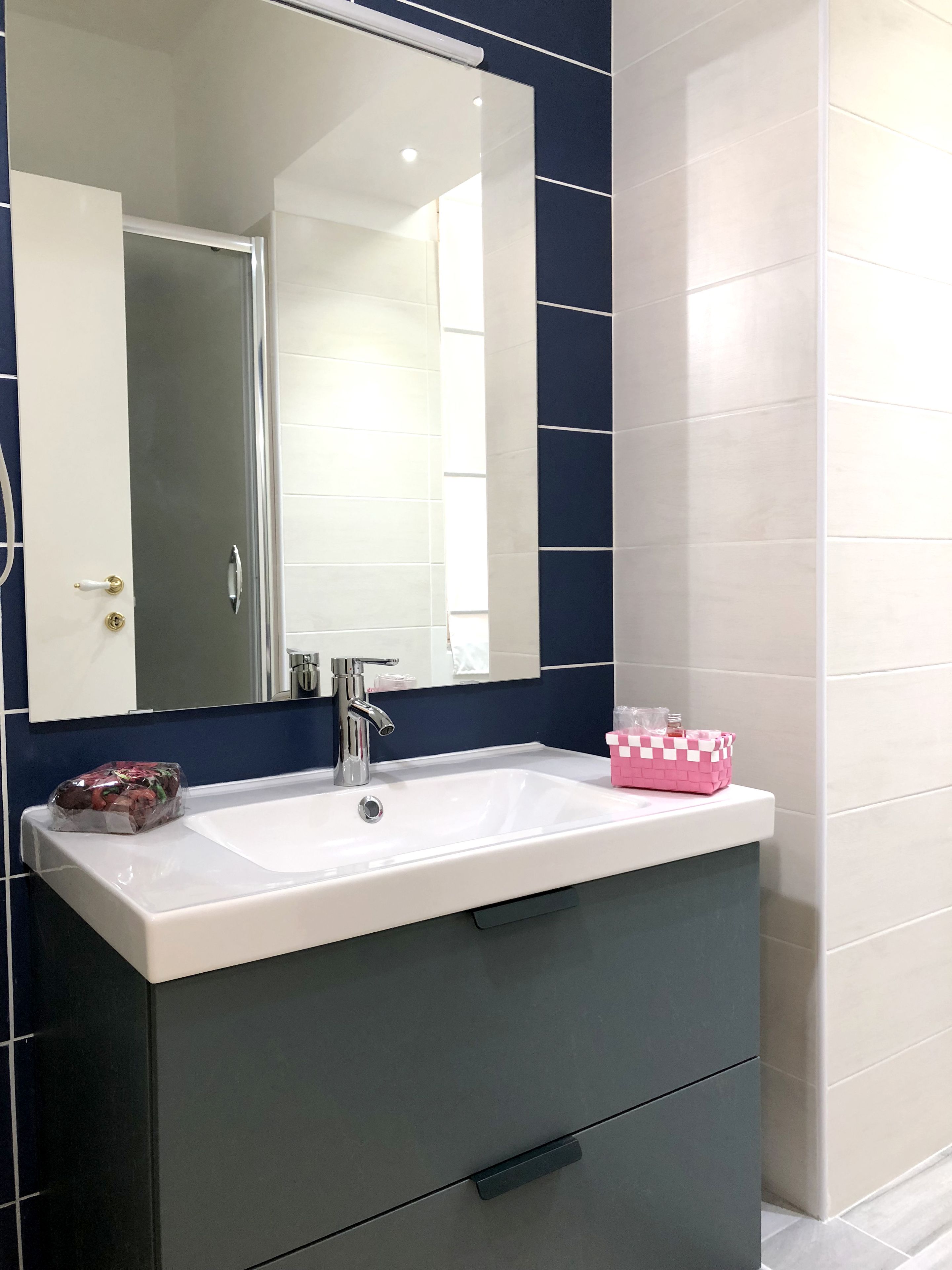 Un baño con un lavamanos blanco, un espejo y una pared de azulejos azul oscuro.