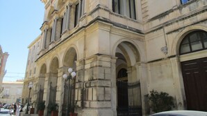 A historic building with classical architecture, featuring arched windows and a prominent entrance with a black iron gate.