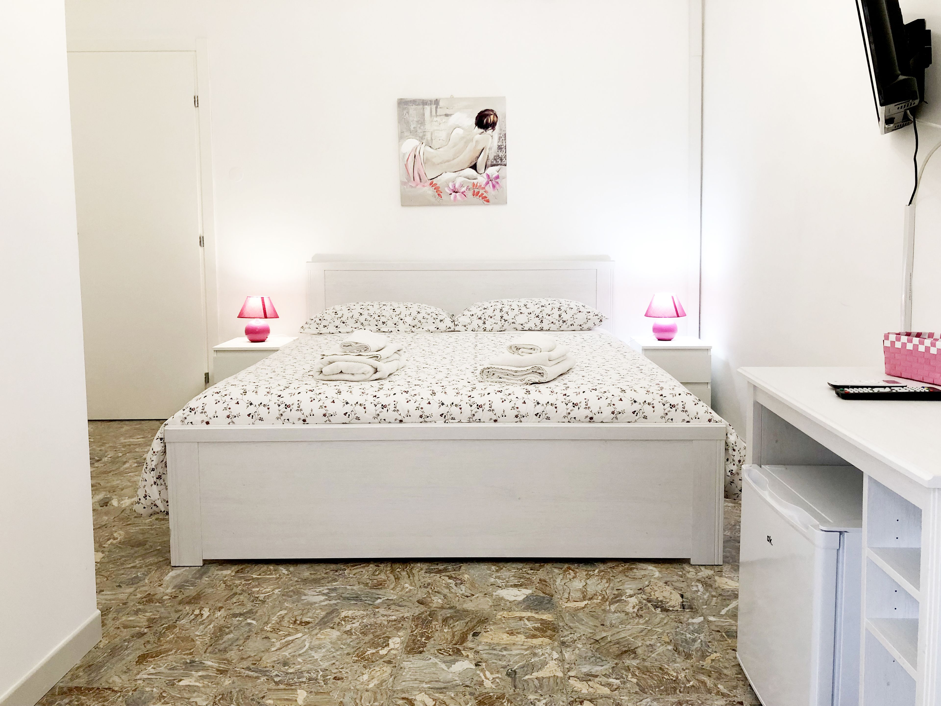 Un dormitorio con una cama, dos lámparas de noche, un escritorio, un televisor y un cuadro en la pared.
