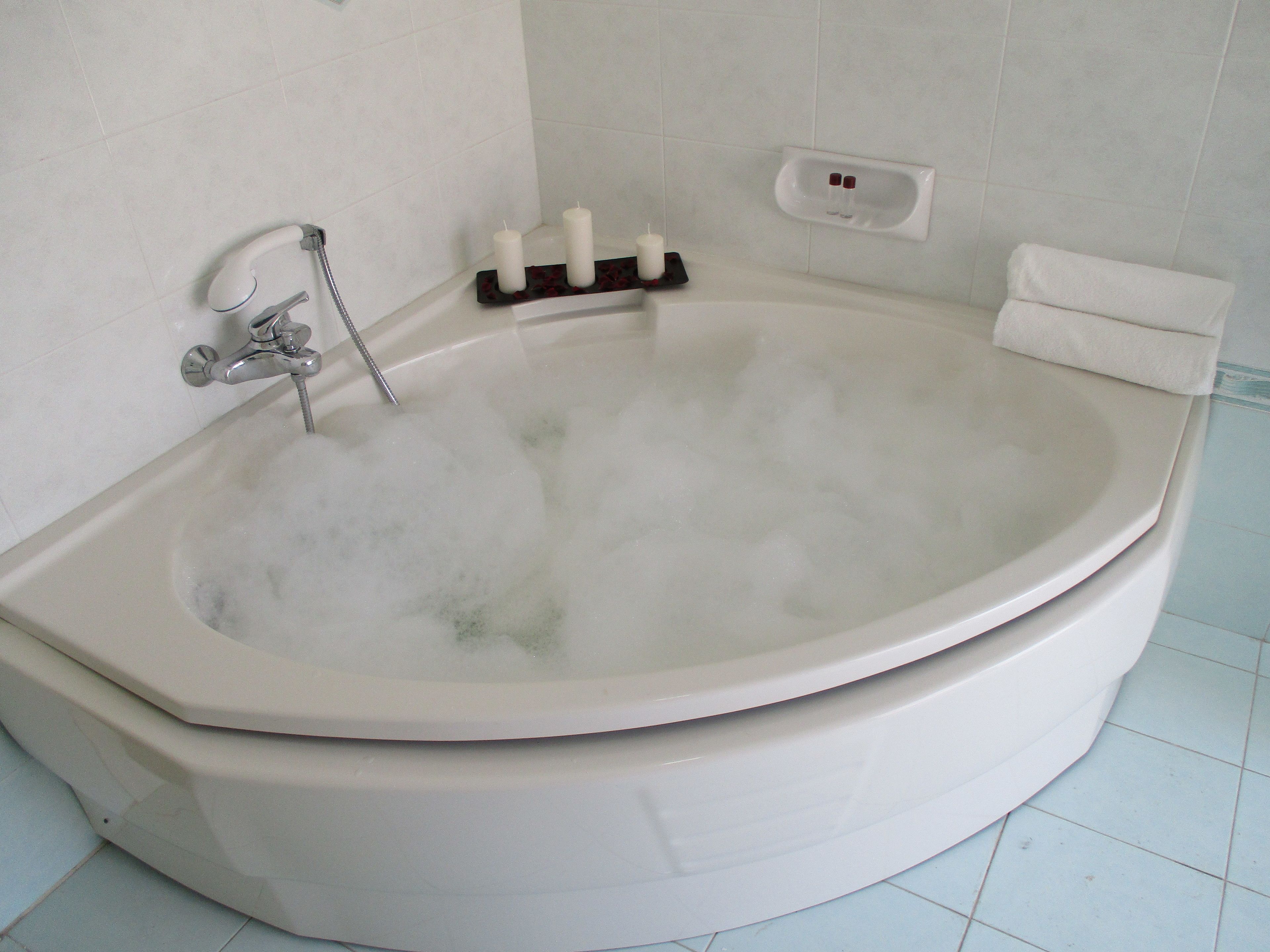 Una bañera blanca llena de burbujas, un cabezal de ducha manual y un jabonera con dos botellas.