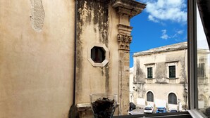 A window with a view of a building with classical architecture, a clear sky, and a vase on the windowsill.