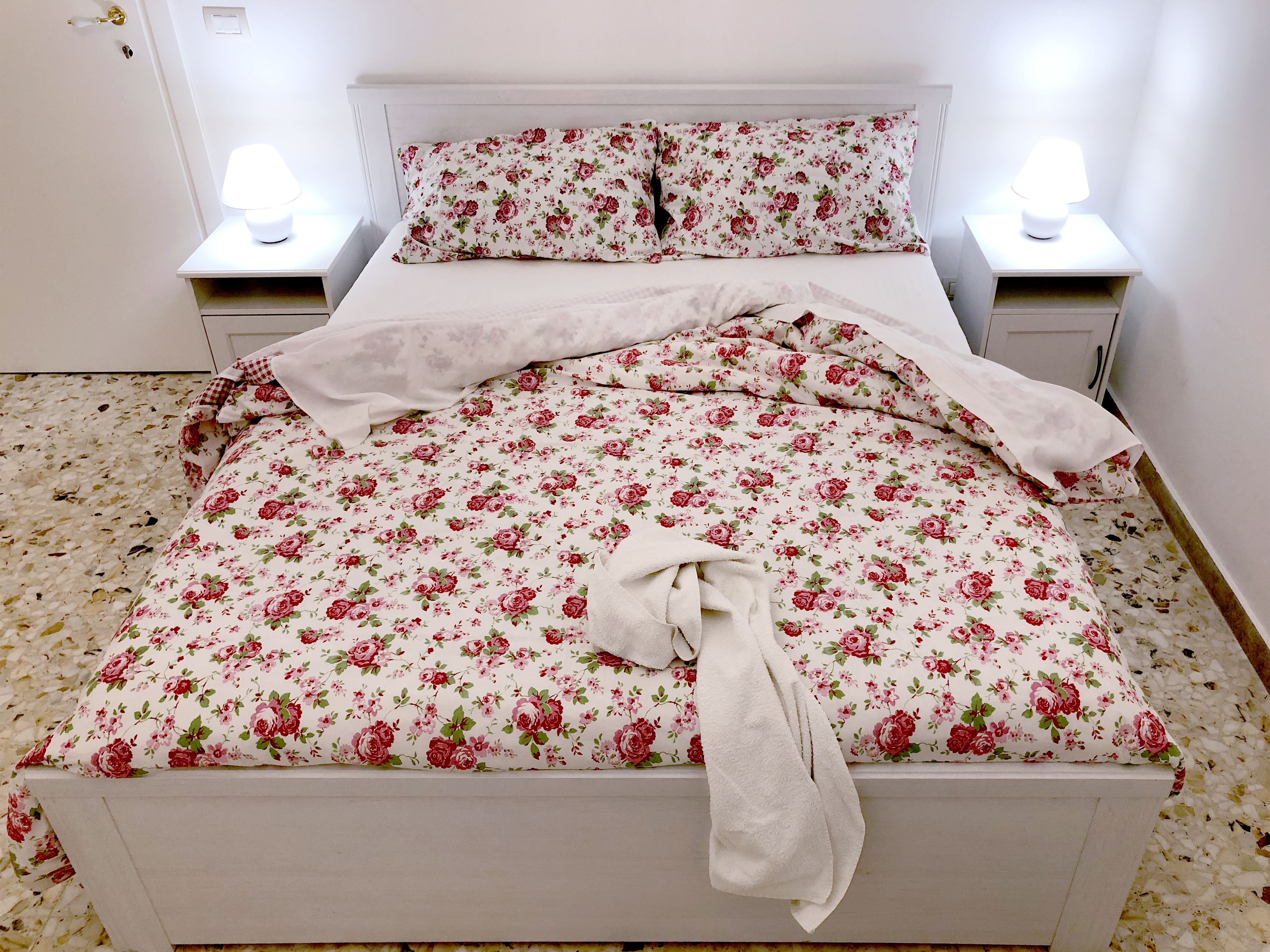 A neatly made bed with floral bedding, two bedside lamps, and a white headboard.