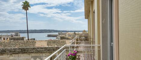 A balcony with a potted plant and a view of a coastal cityscape.