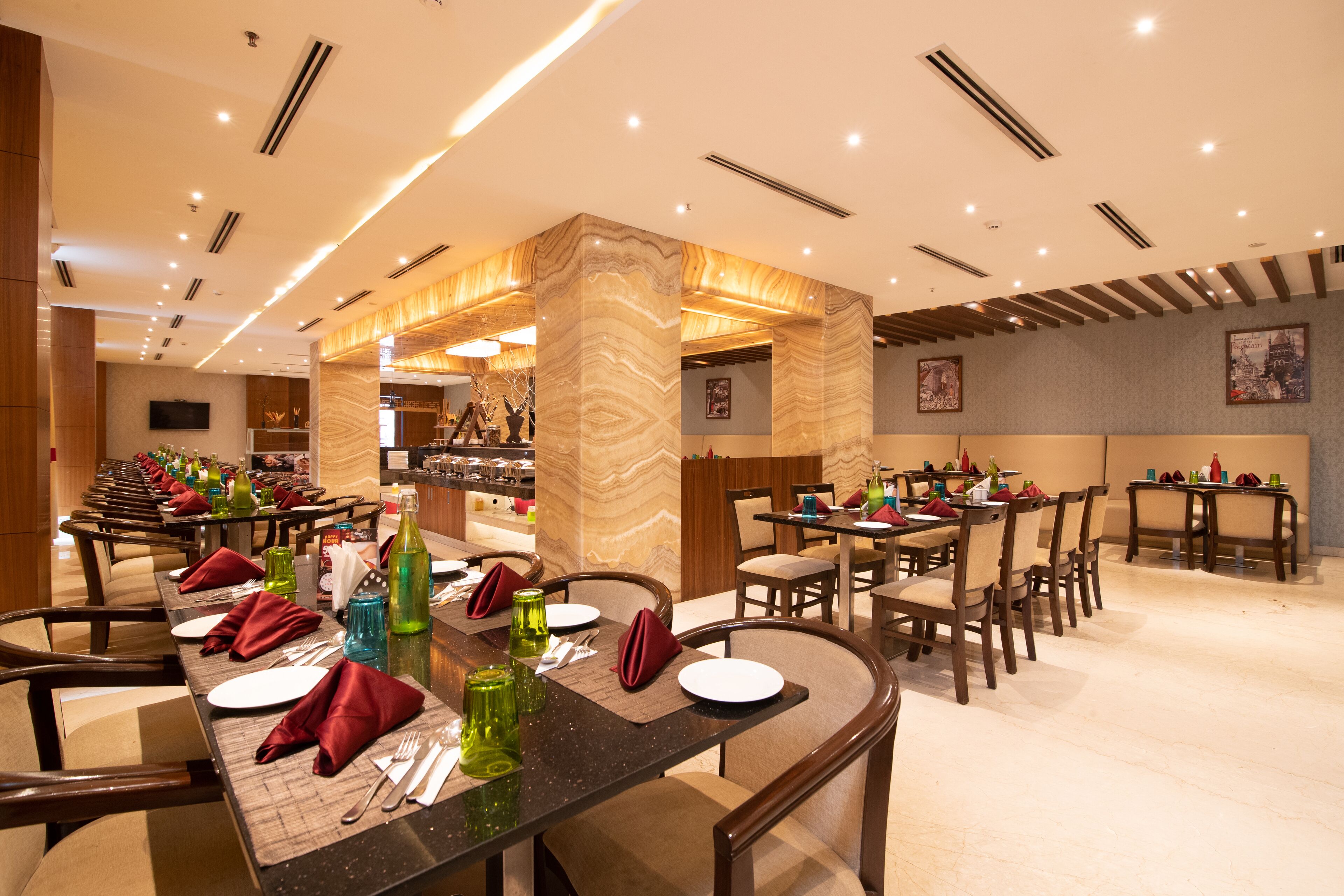 A restaurant with multiple dining tables set with red napkins, cutlery, and green glassware.