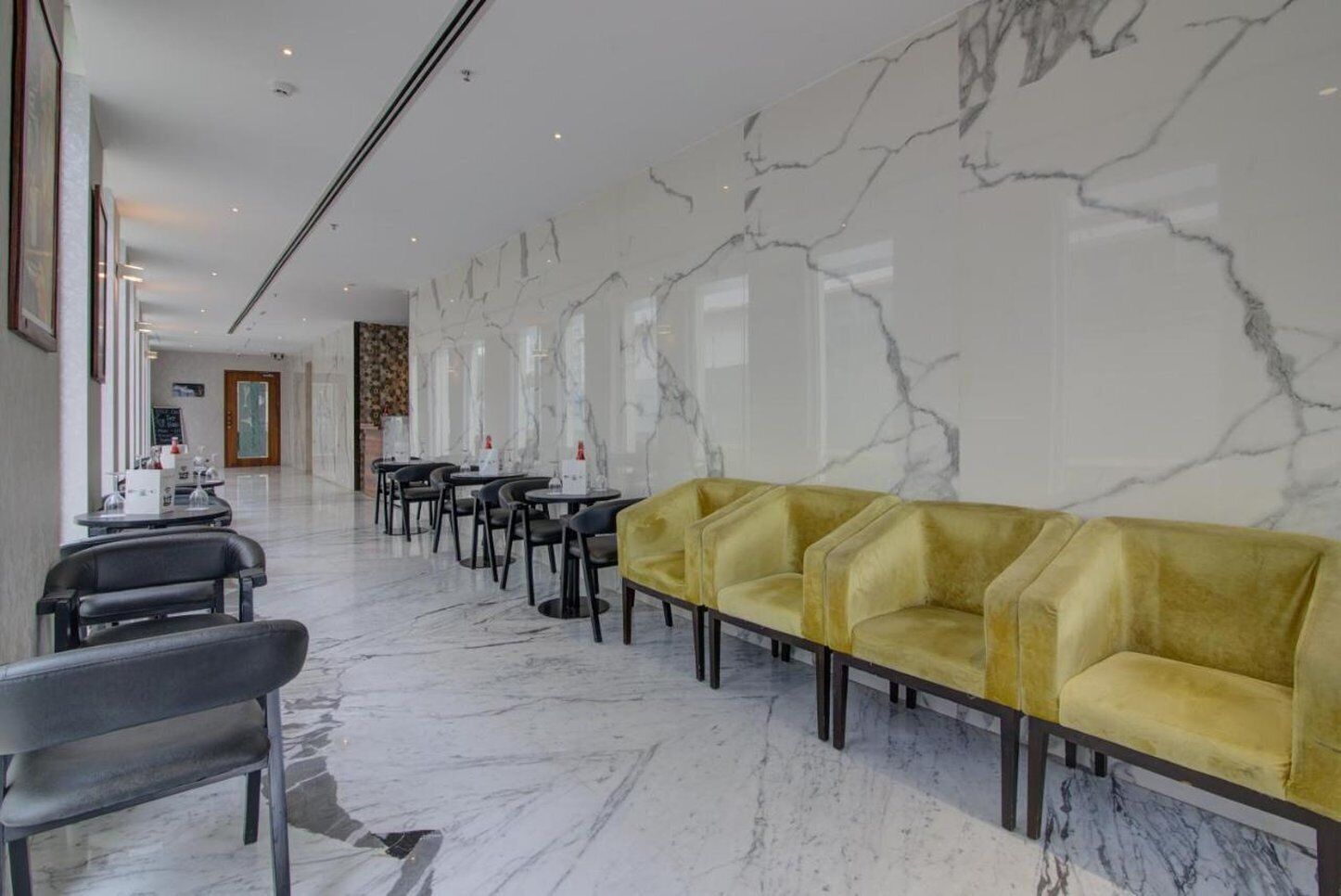 A hotel lobby with marble walls, a yellow sofa, and black chairs.