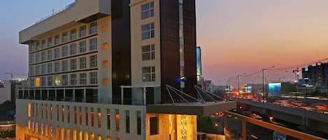 A modern hotel with multiple floors, a rooftop terrace, and a view of the cityscape at dusk.